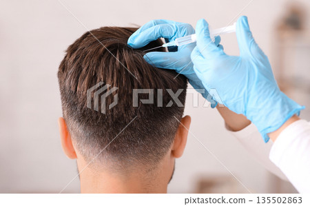 Back view of unrecognizable middle aged man getting hair treatment at beauty salon. Man having mesotherapy session at aesthetic clinic, therapist hands in gloves making injection in scalp, closeup 135502863