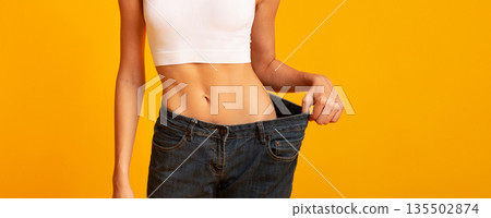 Weight-Loss Comparison. Unrecognizable Girl In Oversize Jeans Standing On Yellow Background. Panorama Weight-Loss Comparison. Unrecognizable Girl In Oversize Jeans Standing On Yellow Background. Panorama 135502874