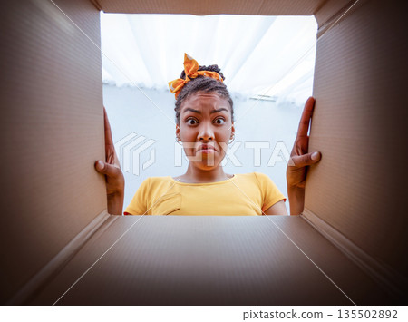 Bad Delivery Service Concept. Angry dissatisfied black woman unpacking and looking in cardboard box, received damaged item, feeling upset with wrong parcel, view from the inside of package 135502892