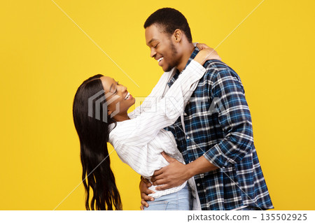 Free time, weekend, date and romance. Smiling young african american man and lady have fun, hug and look at each other, isolated on yellow background, studio shot, profile, copy space, cut out 135502925