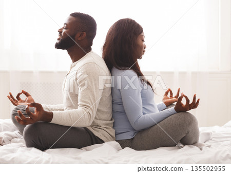 Prenatal yoga. Expecting black woman doing yoga with her husband at home, sitting on back to back with closed eyes Prenatal yoga. Expecting black woman doing yoga with her husband at home, sitting on back to back with closed eyes 135502955