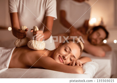 Couple Enjoying Herbal Massage. Relaxed Husband And Wife At Exotic Spa Resort, Lying With Eyes Closed Receiving Thai Massage With Aromatic Bags. Body Beauty Treatment, Relaxation And Wellness Couple Enjoying Herbal Massage. Relaxed Husband And Wife At Exotic Spa Resort, Lying With Eyes Closed Receiving Thai Massage With Aromatic Bags. Body Beauty Treatment, Relaxation And Wellness 135503015