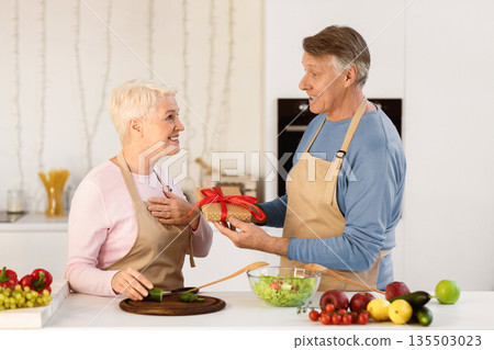 Aged Husband Giving Birthday Gift To Wife Celebrating Family Holiday Or Anniversary In Modern Kitchen At Home. Holidays Celebration, Gifts And Presents, Celebratory Dinner Concept. 135503023
