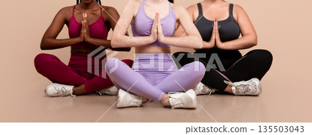 Group Of Three Women With Different Sizes And Skin Types Practicing Yoga Together, Beautiful Body Positive Females In Sportswear Meditating In Studio, Sitting In Lotus Pose Over Beige Background 135503043