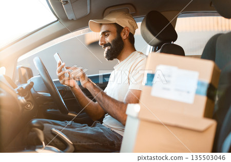 Car Delivery Application. Happy Arabic Deliveryman Texting Via Cellphone Receiving Online Order For Parcel Shipping And Transportation, Sitting Near Carton Boxes In Auto. Selective Focus Car Delivery Application. Happy Arabic Deliveryman Texting Via Cellphone Receiving Online Order For Parcel Shipping And Transportation, Sitting Near Carton Boxes In Auto. Selective Focus 135503046