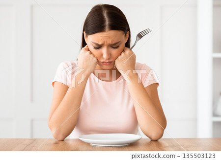 Dieting Concept. Unhappy Woman Looking At Empty Plate Losing Weight Sitting At Table At Home. Dieting Concept. Unhappy Woman Looking At Empty Plate Losing Weight Sitting At Table At Home. 135503123