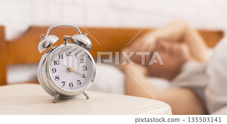 Insomnia problem. Senior woman lying in bed, woke up at 4 am, focus on alarm clock, panorama Insomnia problem. Senior woman lying in bed, woke up at 4 am, focus on alarm clock, panorama 135503141