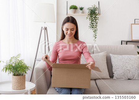 Online store and purchase delivery. Smiling girl received good order in living room interior in daytime, free space Online store and purchase delivery. Smiling girl received good order in living room interior in daytime, free space 135503160
