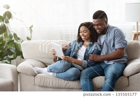 Quarantine Leisure Concept. Happy Black Couple Relaxing With Digital Tablet At Home, Watching Videos Together Or Browsing Internet, Free Space 135503177