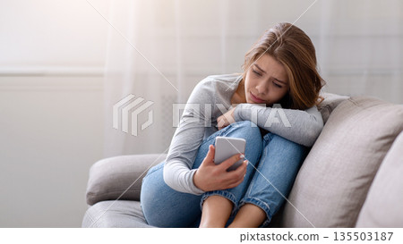 Portrait of sad young woman looking at her smartphone, suffering from cyber bullying or unhappy relationship, going through bad breakup. Depression and emotional problems concept 135503187