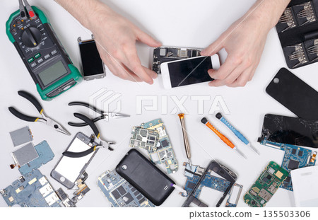 Cell phone repair at service center, smartphone dissasembling and diagnostic, repairman workplace top view Cell phone repair at service center, smartphone dissasembling and diagnostic, repairman workplace top view 135503306