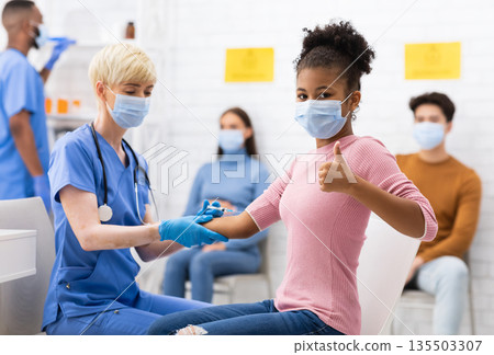 Successful Coronavirus Vaccination. Happy Vaccinated Black Teen Girl Gesturing Thumbs Up After Covid-19 Vaccine Injection In Hospital. Corona Virus Protection And Immunization. Selective Focus Successful Coronavirus Vaccination. Happy Vaccinated Black Teen Girl Gesturing Thumbs Up After Covid-19 Vaccine Injection In Hospital. Corona Virus Protection And Immunization. Selective Focus 135503307