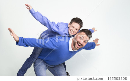 Young father and son playing together, dad riding boy on back, simulating plane, white studio background, panorama 135503308