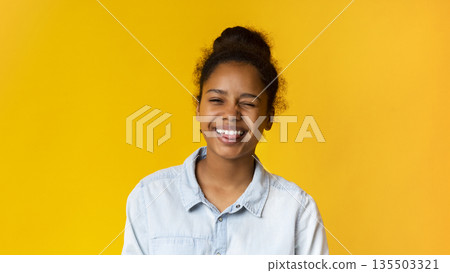 Playful teen girl winking and sticking out tongue on yellow studio background, copy space Playful teen girl winking and sticking out tongue on yellow studio background, copy space 135503321