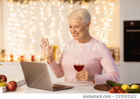 Senior Woman Having Video Call On Christmas Talking With Remote Family Online, Sitting At Laptop In Kitchen At Home, Waving Hello To Webcam And Drinking Wine. Modern Xmas And New Year Celebration Senior Woman Having Video Call On Christmas Talking With Remote Family Online, Sitting At Laptop In Kitchen At Home, Waving Hello To Webcam And Drinking Wine. Modern Xmas And New Year Celebration 135503322
