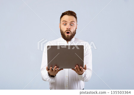 Shocked young businessman in formal wear looking at laptop screen in disbelief on grey studio background. Stunned office worker learning unbelievable news online, learning about huge sale Shocked young businessman in formal wear looking at laptop screen in disbelief on grey studio background. Stunned office worker learning unbelievable news online, learning about huge sale 135503364