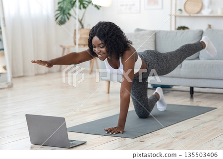 Attractive black woman making morning exercise at home, looking at laptop screen Attractive black woman making morning exercise at home, looking at laptop screen 135503406