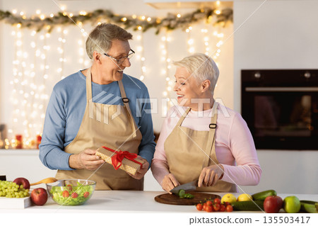 Christmas Celebration. Senior Husband Giving Gift To Wife Surprising Her On Xmas Eve Celebrating Holiday Together In Kitchen At Home. Elderly Spouses Congratulating Each Other On New Year Concept Christmas Celebration. Senior Husband Giving Gift To Wife Surprising Her On Xmas Eve Celebrating Holiday Together In Kitchen At Home. Elderly Spouses Congratulating Each Other On New Year Concept 135503417
