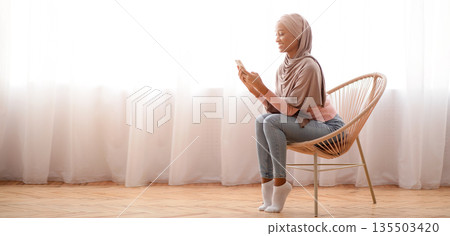 Millennial black lady in hijab using cellphone at home, working or studying remotely, free space. African American woman in Muslim headscarf checking email, sending message, having online video call Millennial black lady in hijab using cellphone at home, working or studying remotely, free space. African American woman in Muslim headscarf checking email, sending message, having online video call 135503420
