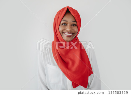 Portrait of happy african american muslim woman in hijab looking and smiling at camera, standing over light studio background. Positive black lady in headscarf 135503529