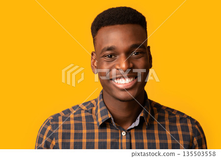 Closeup portrait of positive young African American guy sincerely smiling at camera, cheerful black millennial student guy in checkered shirt standing isolated over yellow background, free space 135503558