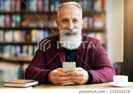 Cheerful elderly grey-haired man with long beard using modern mobile phone while drinking coffee at cafe, chatting with his family or business partners, having notebook by him, free space Cheerful elderly grey-haired man with long beard using modern mobile phone while drinking coffee at cafe, chatting with his family or business partners, having notebook by him, free space 135503578
