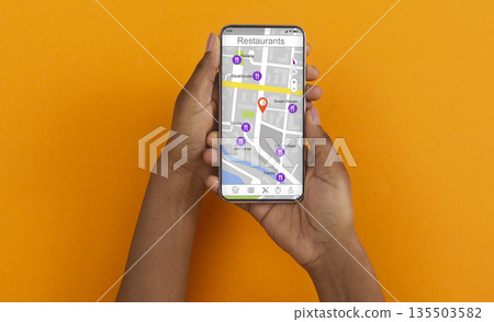 African American girl holding cellphone with map and restaurant navigation pointers on screen, orange background. Collage. Panorama 135503582