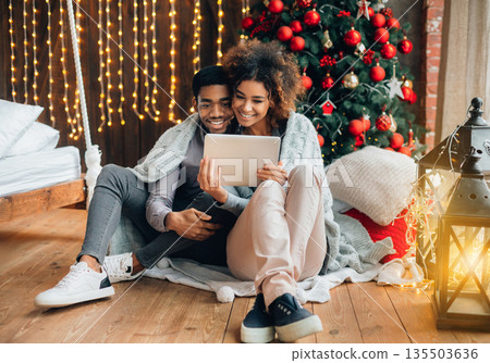 Happy millennial couple browsing on digital tablet at Christmas eve, sitting at home together 135503636