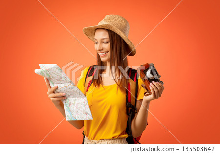 Happy girl traveller with camera looking at map, yellow studio background 135503642