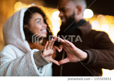Love, Affection And Bonding Concept. Closeup outdoor portrait of happy smiling black african american couple making heart shape with hands walking together in the evening, looking at each other 135503652