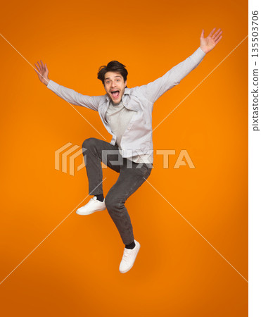 Funny man jumping with raised arms over orange studio background Funny man jumping with raised arms over orange studio background 135503706