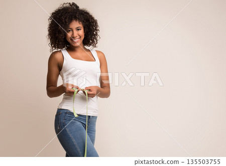 Happy african-american woman measuring waist with tape over light background Happy african-american woman measuring waist with tape over light background 135503755