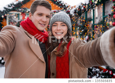 Happy lovers young man and woman taking selfie while spending winter holidays at backyard together, loving millennial couple celebrating Christmas, New Year, decorated street background Happy lovers young man and woman taking selfie while spending winter holidays at backyard together, loving millennial couple celebrating Christmas, New Year, decorated street background 135503835