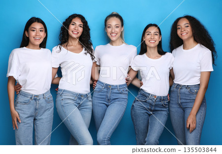 Multiethnic Beauty. Diverse Girls Embracing Posing On Blue Studio Background, Smiling To Camera Multiethnic Beauty. Diverse Girls Embracing Posing On Blue Studio Background, Smiling To Camera 135503844