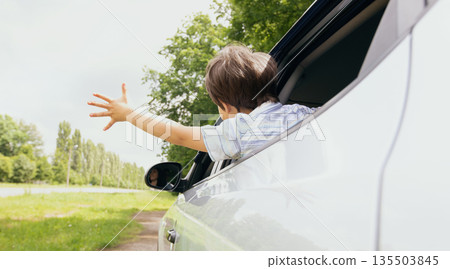 Rear view of little boy leaning out of car window and trying to catch wind with outstretched hand, small male child enjoying summer weather and automobile ride, on the move shot, closeup Rear view of little boy leaning out of car window and trying to catch wind with outstretched hand, small male child enjoying summer weather and automobile ride, on the move shot, closeup 135503845