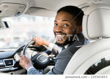 Young afro businessman at driver's seat smiling to camera over shoulder, free space Young afro businessman at driver's seat smiling to camera over shoulder, free space 135503853