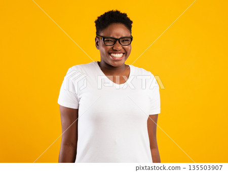 Overweight African Woman's Portrait. Positive Plus Size Black Lady Posing Smiling To Camera Standing Over Yellow Studio Background, Wearing Glasses. Shot Of Happy Female With Short Haircut Overweight African Woman's Portrait. Positive Plus Size Black Lady Posing Smiling To Camera Standing Over Yellow Studio Background, Wearing Glasses. Shot Of Happy Female With Short Haircut 135503907