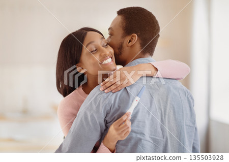 African American man embracing his happy young wife with positive pregnancy test indoors. Millennial black couple expecting baby. Maternity and childbearing concept African American man embracing his happy young wife with positive pregnancy test indoors. Millennial black couple expecting baby. Maternity and childbearing concept 135503928