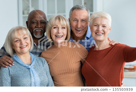 Multiracial group of cheerful positive senior people men and women in casual outfits taking selfie together while having home party, hugging and smiling at camera, kitchen interior 135503939