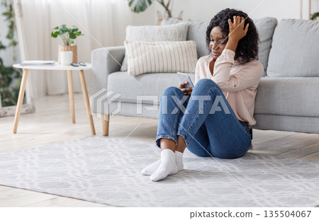 Heartbroken Girl. Upset Crying Black Woman Sitting With Smartphone On Floor At Home, Feeling Lonely And Depressed After Brokeup With Boyfriend Heartbroken Girl. Upset Crying Black Woman Sitting With Smartphone On Floor At Home, Feeling Lonely And Depressed After Brokeup With Boyfriend 135504067