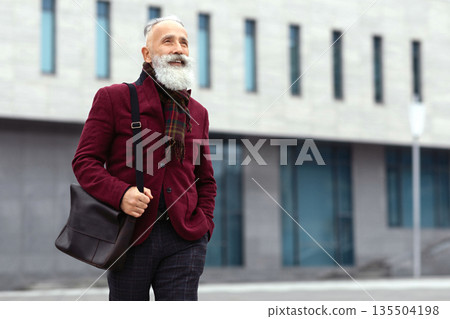 Happy senior grey-haired man in stylish burgundy jacket walking by street alone, going home from job, smiling and looking at copy space. Working during retirement concept, lifestyle of elderly Happy senior grey-haired man in stylish burgundy jacket walking by street alone, going home from job, smiling and looking at copy space. Working during retirement concept, lifestyle of elderly 135504198
