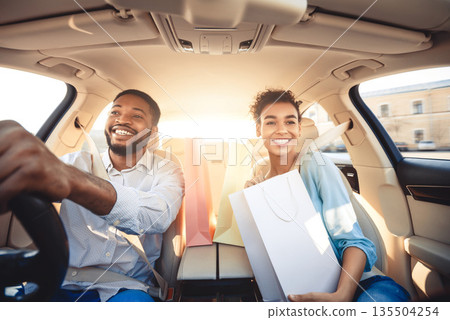 Go home after shopping. Couple driving home in car with paper bags, listening music and smiling Go home after shopping. Couple driving home in car with paper bags, listening music and smiling 135504254