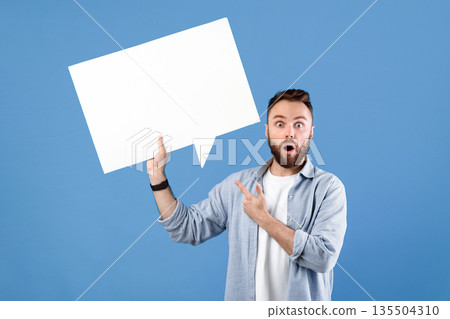Shocked young guy pointing at empty speech bubble with space for your design over blue studio background, mockup. Attractive bearded man with blank word cloud. Chat, dialog, announcement concept Shocked young guy pointing at empty speech bubble with space for your design over blue studio background, mockup. Attractive bearded man with blank word cloud. Chat, dialog, announcement concept 135504310