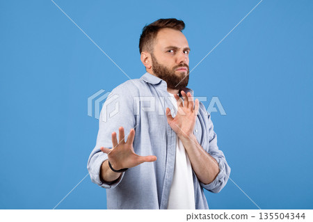 Repulsed millennial guy rejecting something, making STOP gesture over blue studio background. Revolted young man feeling disgusted, expressing rejection or dislike 135504344