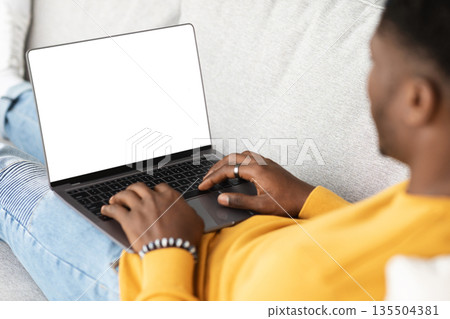 Unrecognizable black guy using modern laptop with empty screen, typing on computer keyboard, reclining on couch, using nice software, programming, chatting with ladies, cropped, mockup Unrecognizable black guy using modern laptop with empty screen, typing on computer keyboard, reclining on couch, using nice software, programming, chatting with ladies, cropped, mockup 135504381