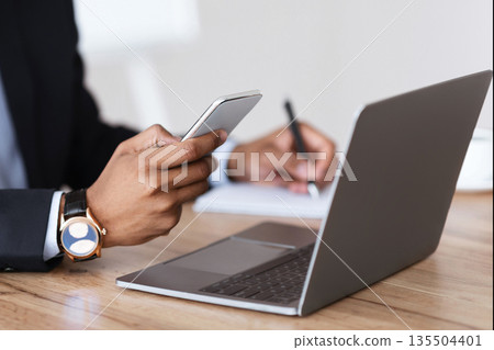 Unrecognizable black manager in suit holding smartphone, taking notes, sitting in front of laptop, office interior, cropped. African american businessman using modern gadgets for business Unrecognizable black manager in suit holding smartphone, taking notes, sitting in front of laptop, office interior, cropped. African american businessman using modern gadgets for business 135504401