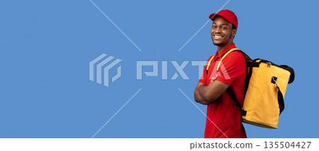 Delivery Service Cocnept. Portrait of confident smiling black male courier wearing red uniform and thermo backpack bag posing with folded arms and looking at camera isolated on blue studio background Delivery Service Cocnept. Portrait of confident smiling black male courier wearing red uniform and thermo backpack bag posing with folded arms and looking at camera isolated on blue studio background 135504427