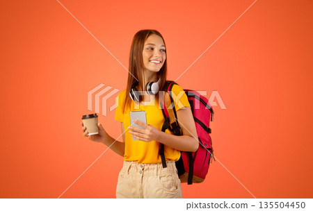 Active young woman with backpack and smartphone holding coffee to go and looking at copy space, yellow studio background. Female traveller using mobile app city guide and drinking tea Active young woman with backpack and smartphone holding coffee to go and looking at copy space, yellow studio background. Female traveller using mobile app city guide and drinking tea 135504450