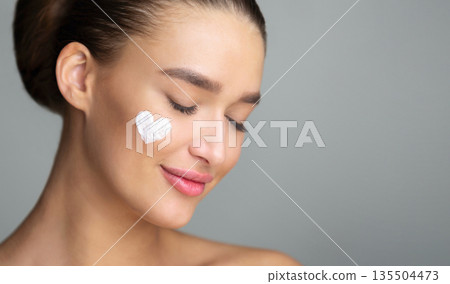 Woman with Cream In Heart Shape On Cheek, Grey Studio Background Woman with Cream In Heart Shape On Cheek, Grey Studio Background 135504473