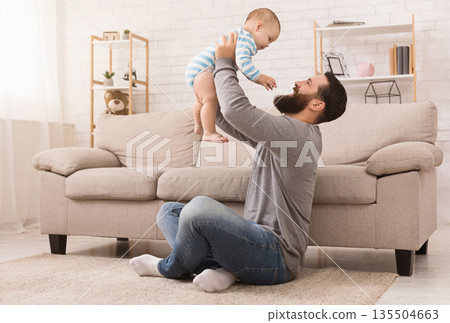 Father and kid spending time together, man throwing up his son at home in living room, copy space Father and kid spending time together, man throwing up his son at home in living room, copy space 135504663